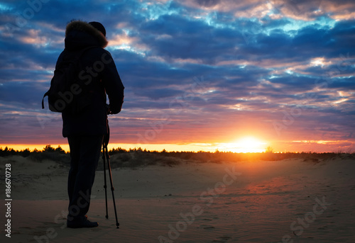 The photographer shoots landscapes during the sunset on the sand. Beautiful colorful sunrise sky. Creativity and success.