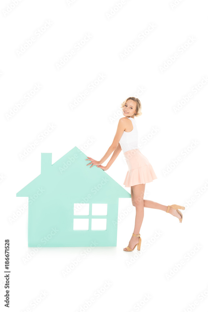 young smiling woman standing near house model isolated on white young smiling woman standing near house model isolated on white