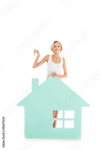 young woman with keys in hand standing near house model isolated on white