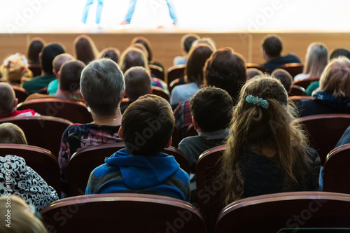 People, parents with children in the audience watching a children's show. Sold out. Shooting from the back.