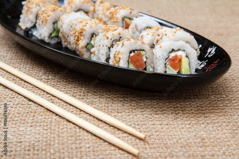 Uramaki sushi rolls with avocado and red fish on ceramic plate and wooden sticks Uramaki sushi rolls with avocado and red fish on ceramic plate and wooden sticks