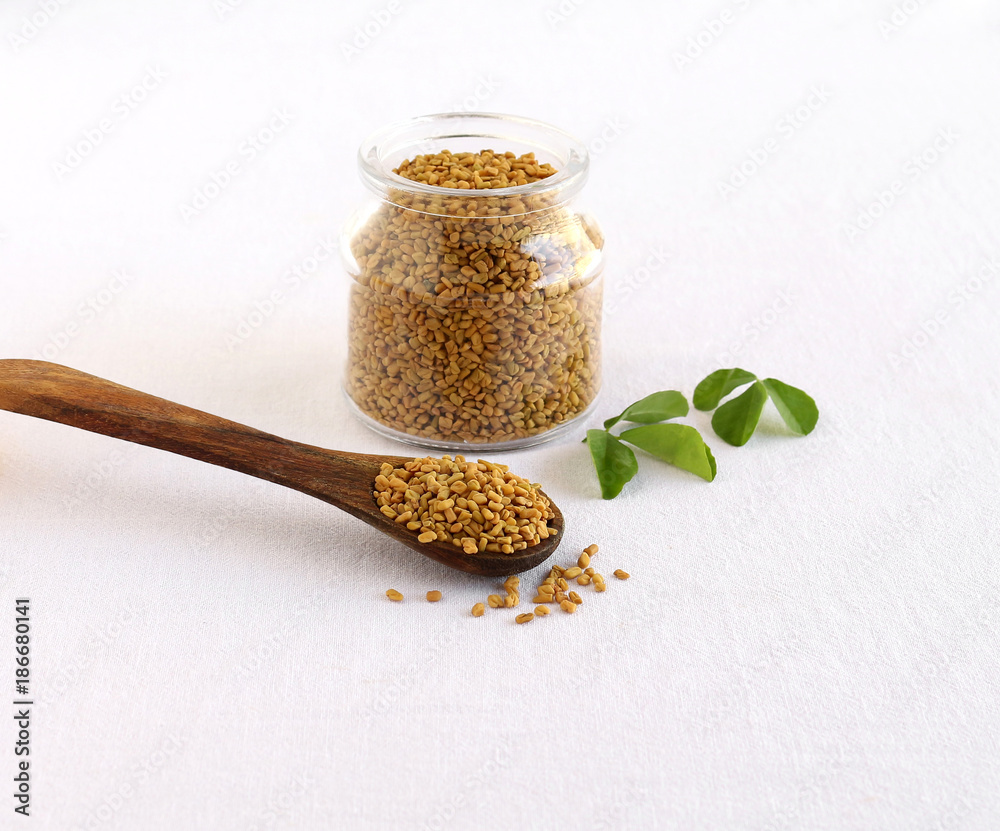 Φωτογραφία Methi or fenugreek seeds in a wooden spoon and in the background is a bottle of the same seeds and next to the bottle are methi leaves
