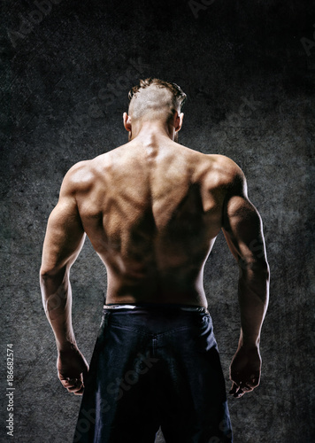 Back view. Naked torso of muscular man on dark background. Strength and motivation