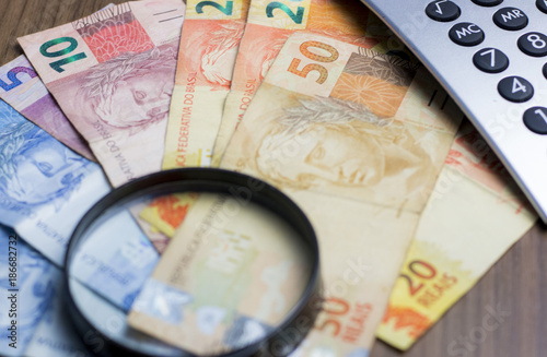 Notas de dinheiro acompanhado de moedas, carteira de trabalho, lupa, calculadora encima da mesa photo
