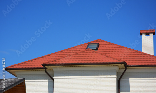 House with metal roof tiles, attic skylight windows. Home Guttering, roof gutters, plastic guttering system. © bildlove