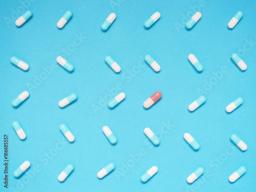 Unique brown capsule among many blue and white capsule on blue background. Creative idea for uniqueness, innovation, different thinking, individuality, contrast and pharmaceutical concept.