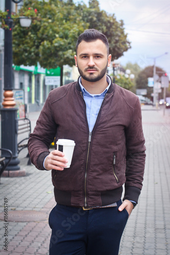 Man in a jacket and suit on a European street with coffee in his hands. Business guy fashion clothes. Autumn landscape, portrait. stock photo
