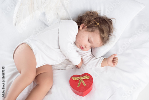 little cherub with wings lying on bed with gift box