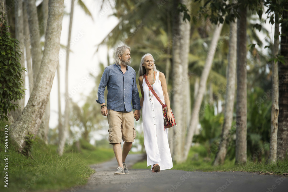 Handsome senior couple strolling through tropical landscape with palm trees Handsome senior couple strolling through tropical landscape with palm trees