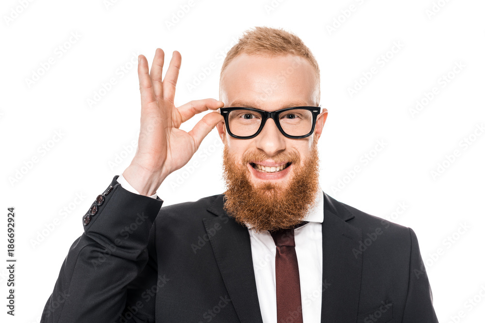bearded young businessman adjusting eyeglasses and smiling at camera isolated on white bearded young businessman adjusting eyeglasses and smiling at camera isolated on white