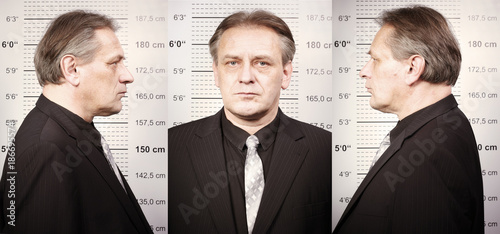 Older criminal man portraited in police station style in front of mug board photo