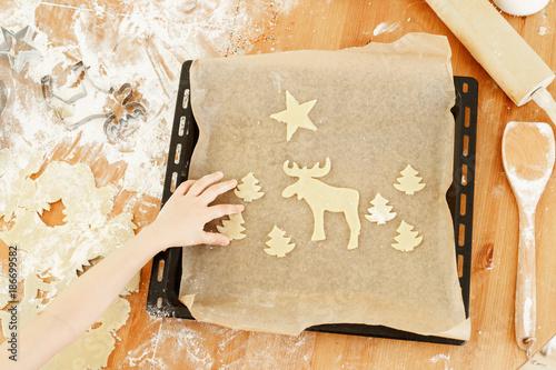 Unrecognizable child puts ready hand made cookies on baking tray, helps mother with preparation for Christmas. Butter Christmas cookies. Tasty ginger bread. photo