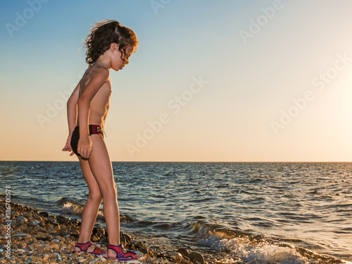 Baby boy barefoot are walking on the beach in water. Child on vacation in summer at the sea at sunset. © kravik93