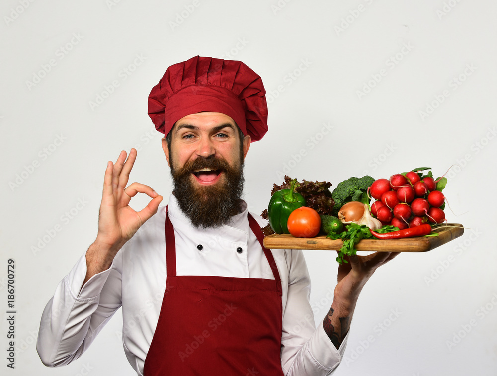 Cook with happy face in burgundy uniform holds salad ingredients Cook with happy face in burgundy uniform holds salad ingredients