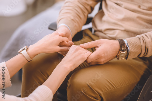 cropped image of husband on wheelchair and wife holding hands