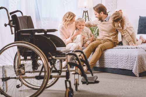 happy father with disability and mother sitting with children on bed