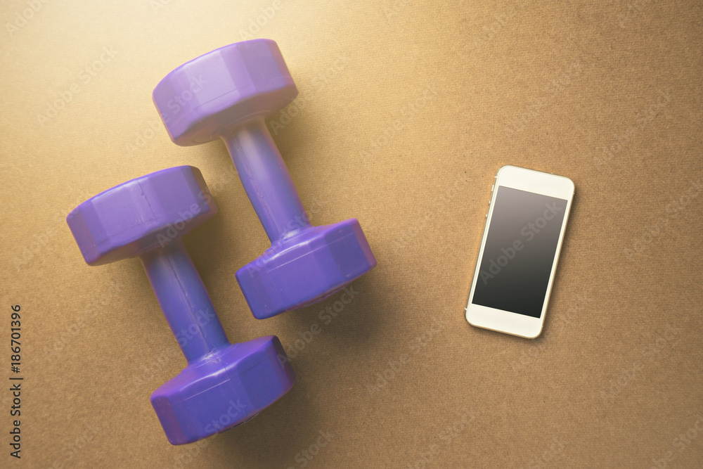 Flat lay design For healthy sport with mobile phone and 2 purple dumbbell on wooden background. Flat lay design For healthy sport with mobile phone and 2 purple dumbbell on wooden background.