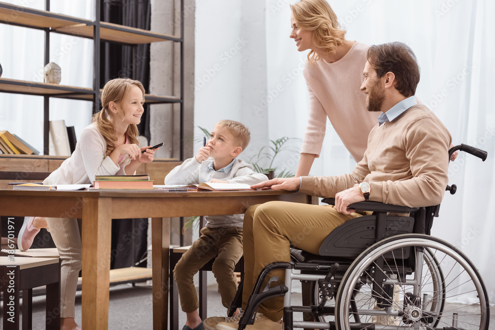 smiling father on wheelchair and mother teaching children at home smiling father on wheelchair and mother teaching children at home