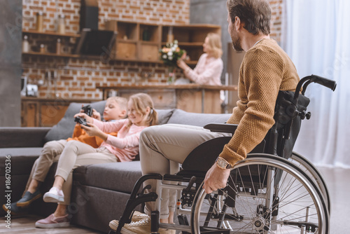 father on wheelchair looking how happy children playing video game