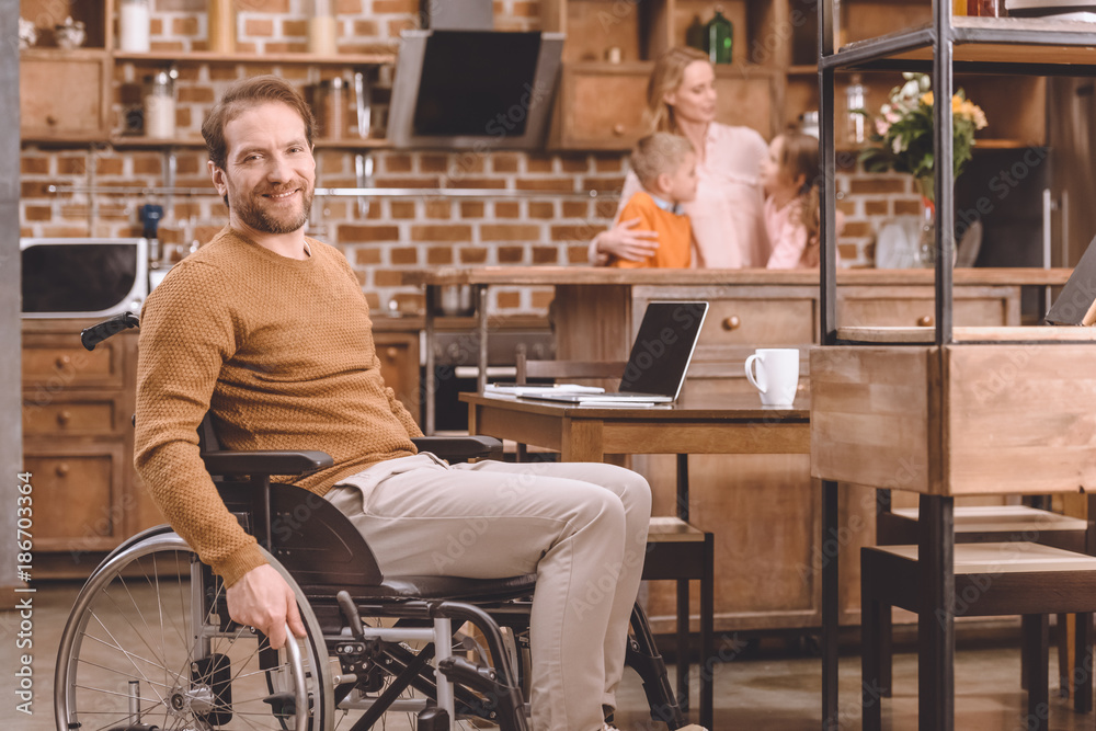 disabled middle aged man in wheelchair smiling at camera while spending time with family at home disabled middle aged man in wheelchair smiling at camera while spending time with family at home
