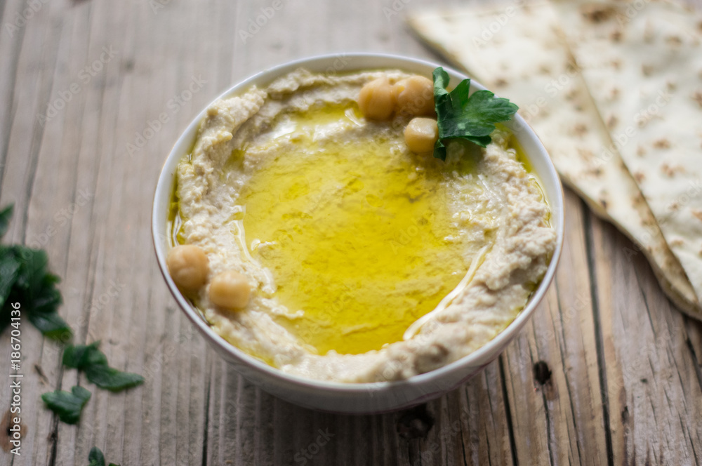 Homemade arabic hummus with parsley in a little white bowl on a wooden table with arabic bread on a side Homemade arabic hummus with parsley in a little white bowl on a wooden table with arabic bread on a side