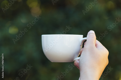 Woman hand holding a cup of coffee in the morning, with nature background. Relaxing and healthy concept.