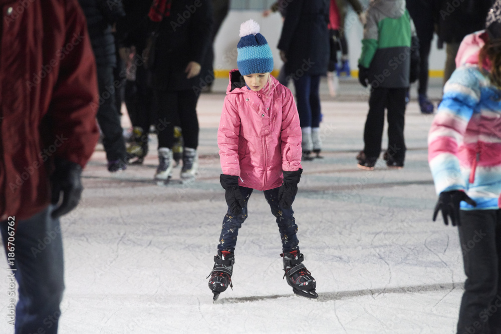 Child young girl ice skating at the ice rink outdoors. Child learning to skate on public rink. Ice skaters using a temporary rink during the Christmas and New Year holiday period Child young girl ice skating at the ice rink outdoors. Child learning to skate on public rink. Ice skaters using a temporary rink during the Christmas and New Year holiday period