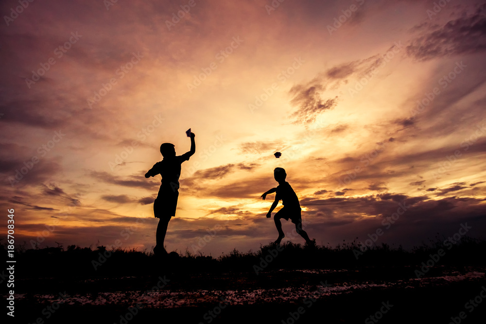 Silhouette of children playing paper airplane at sunset