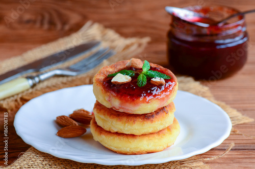 Sweet cottage cheese pancakes with berry jam, almonds nuts and fresh mint on a serving plate. Simple breakfast pancakes recipe. Closeup photo