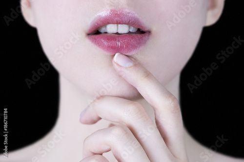 Close up of a young woman s pink lips with white teeth and hand gently touching her chin on black background