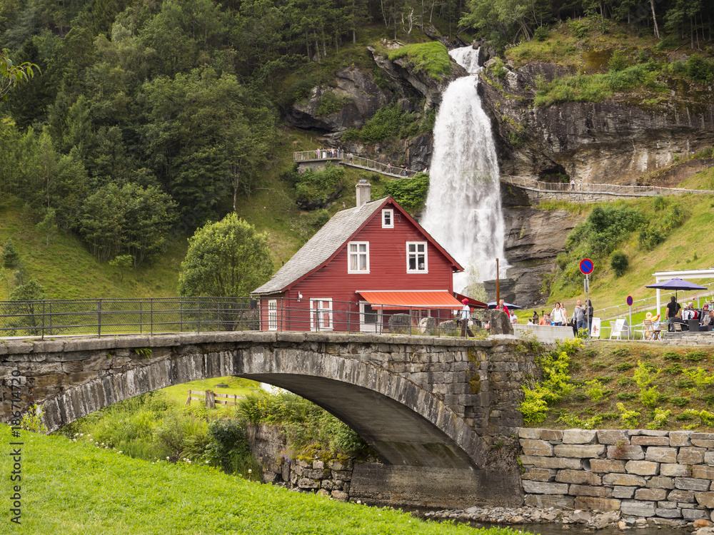 Norheimsund, norte del Hardangerfjord, donde se ubica la impresionante cascada  Steinsdalsfossen, rodeada de vegetación con un puente y una casita roja  típica Noruega, en el verano de 2017 foto de Stock
