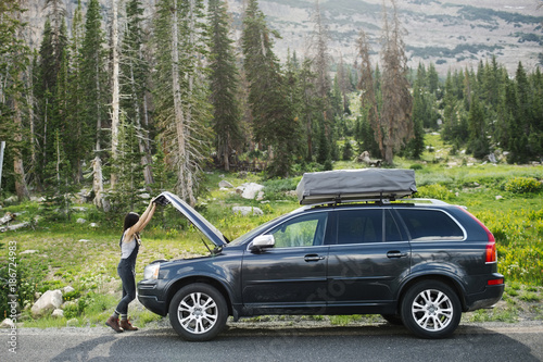 Side view of woman opening a car hood in the forest photo