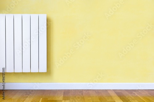 Billede på lærred Modern white electric heater mounted on a yellow wall in a room with wooden floor and white baseboard
