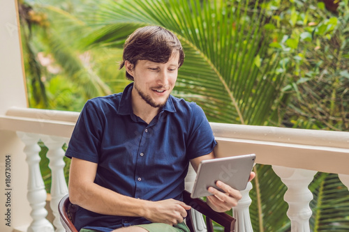 man in tropics talking with friends and family on video call using a tablet and wireless headphones photo