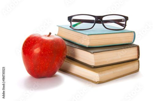 Three old books, glasses and a red apple on a white background