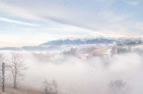 Winter landscape in the mountains. Rural landscape in the evening with fog and clouds on the sky. There are some houses in the image. © Lucian Bolca
