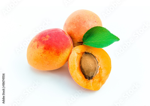Fresh ripe apricots, whole and half, with leaves, on white background.