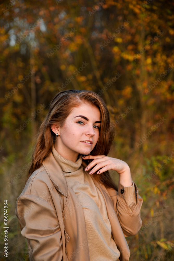 Stylish and beautiful red haired girl posing, walking in autumn forest among yellow grass. Woman with long hair, in jeans, blouse and brown coat, smiling, relaxing outdoors. Stylish and beautiful red haired girl posing, walking in autumn forest among yellow grass. Woman with long hair, in jeans, blouse and brown coat, smiling, relaxing outdoors.