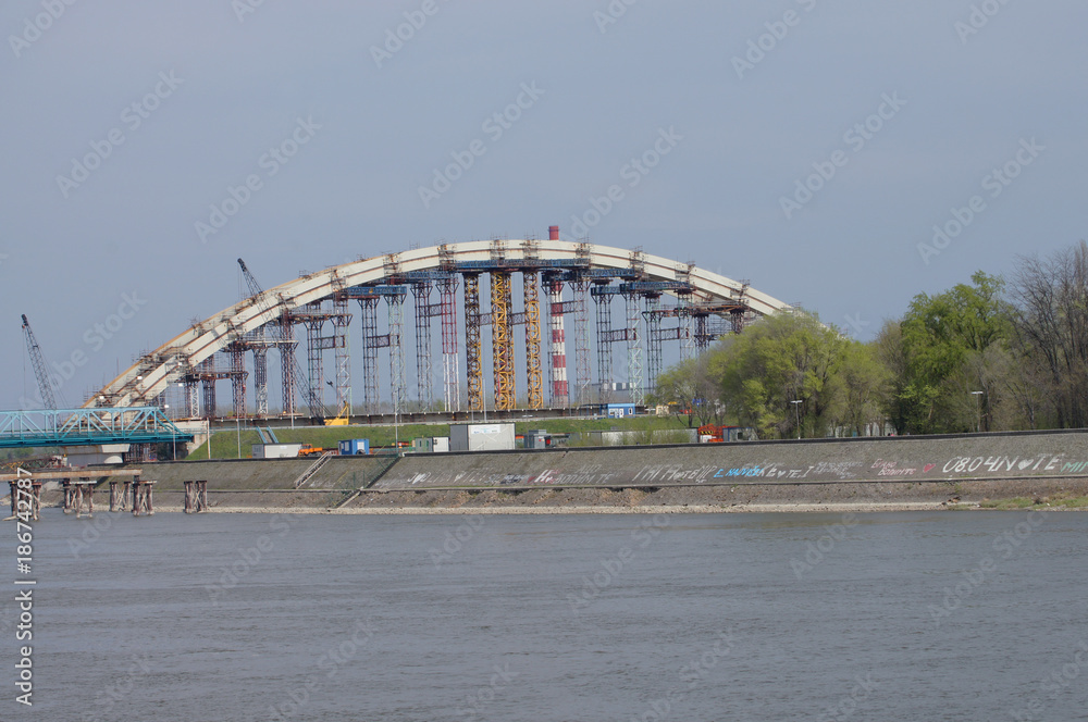 Obraz premium The arch of the bridge under construction. Carriers ensure arch stability. Facing architectural solutions of the old and the new bridge. The inscriptions are found on rocky shore of the river. 
