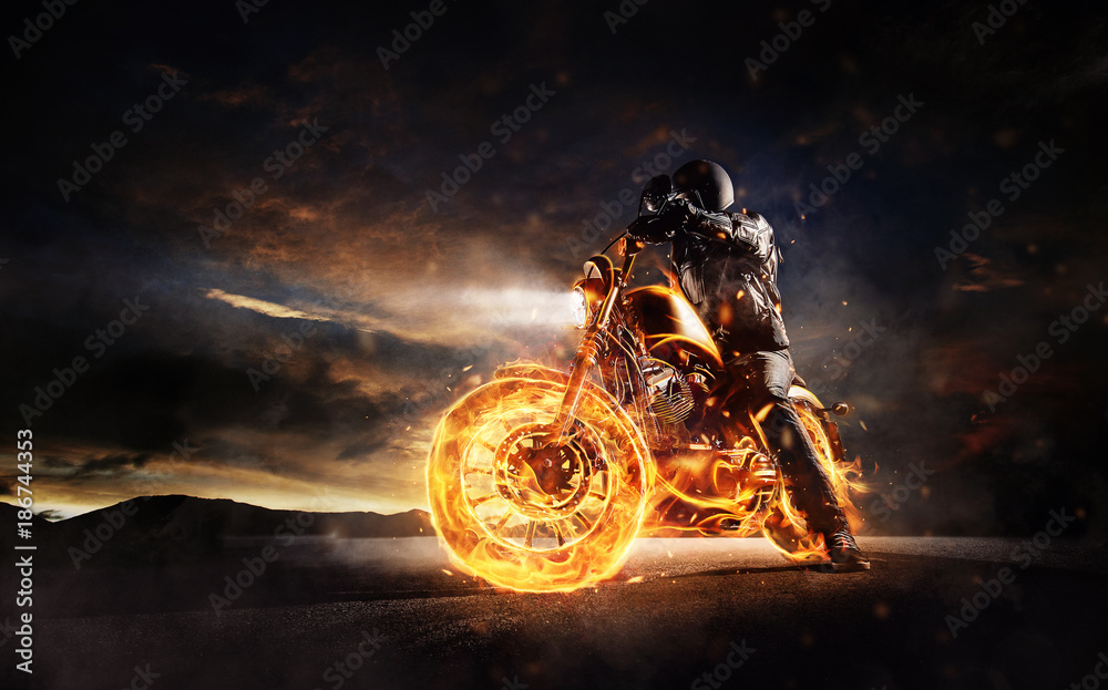 Fototapeta premium Ciemny motorbiker zostaje na płonącym motocyklu w zmierzchu świetle