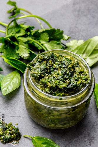 Chimichurri sauce. Argentine green parsley basil sauce chimichurri for barbecue asado in glass jar, gray slate background photo