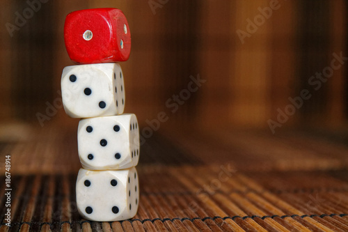 Stack of three white plastic dices and one red dice on brown wooden board background. Six sides cube with black dots. Number 1, 3, 4, 5
