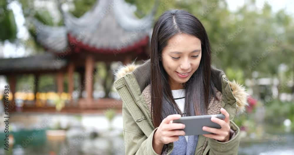 Woman play excited game on mobile phone in chinese garden
