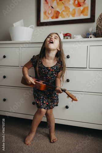 Full length of girl playing guitar while standing at home