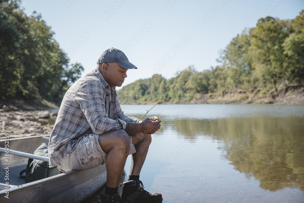 Man adjusting fishing tackle while sitting on boat by lake Photos