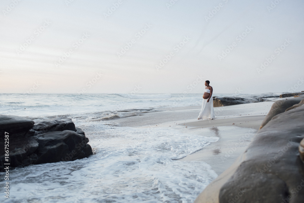 Pregnant woman walking at beach against sky during sunset Pregnant woman walking at beach against sky during sunset