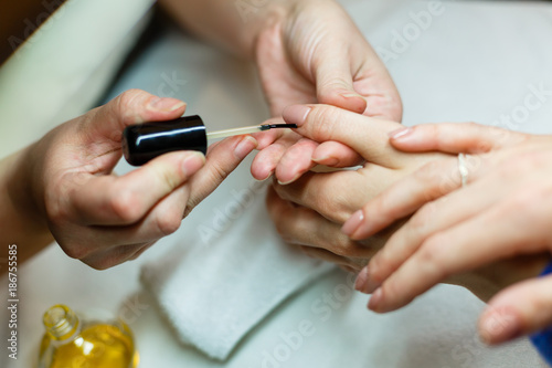 The master does a manicure in the salon, close-up. He paints his nails with white lacquer. © Angelov