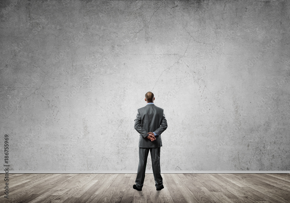 Businessman with hands behind his back and looking at blank concrete wall Businessman with hands behind his back and looking at blank concrete wall