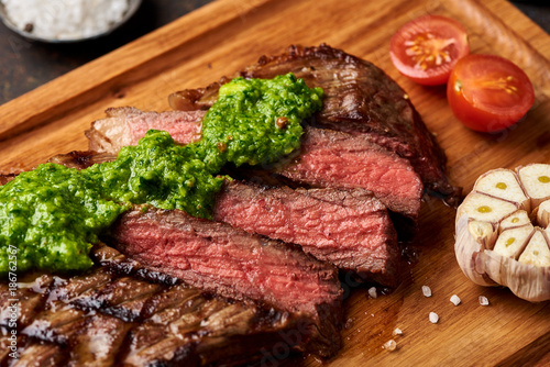 Grilled Black Angus Steak with tomatoes, garlic with chimichurri sauce on meat cutting board. photo