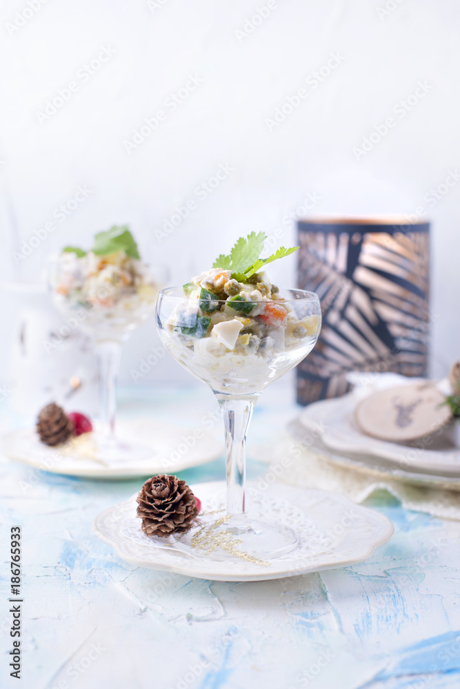 traditional New Year's Russian salad of vegetables and meat, with mayonnaise. Served in a glass and decorated with parsley, on a white table